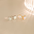 Two pairs of Princess Cut Opal Studs—one silver, one gold—bring vintage-inspired elegance as they shimmer on a reflective surface.