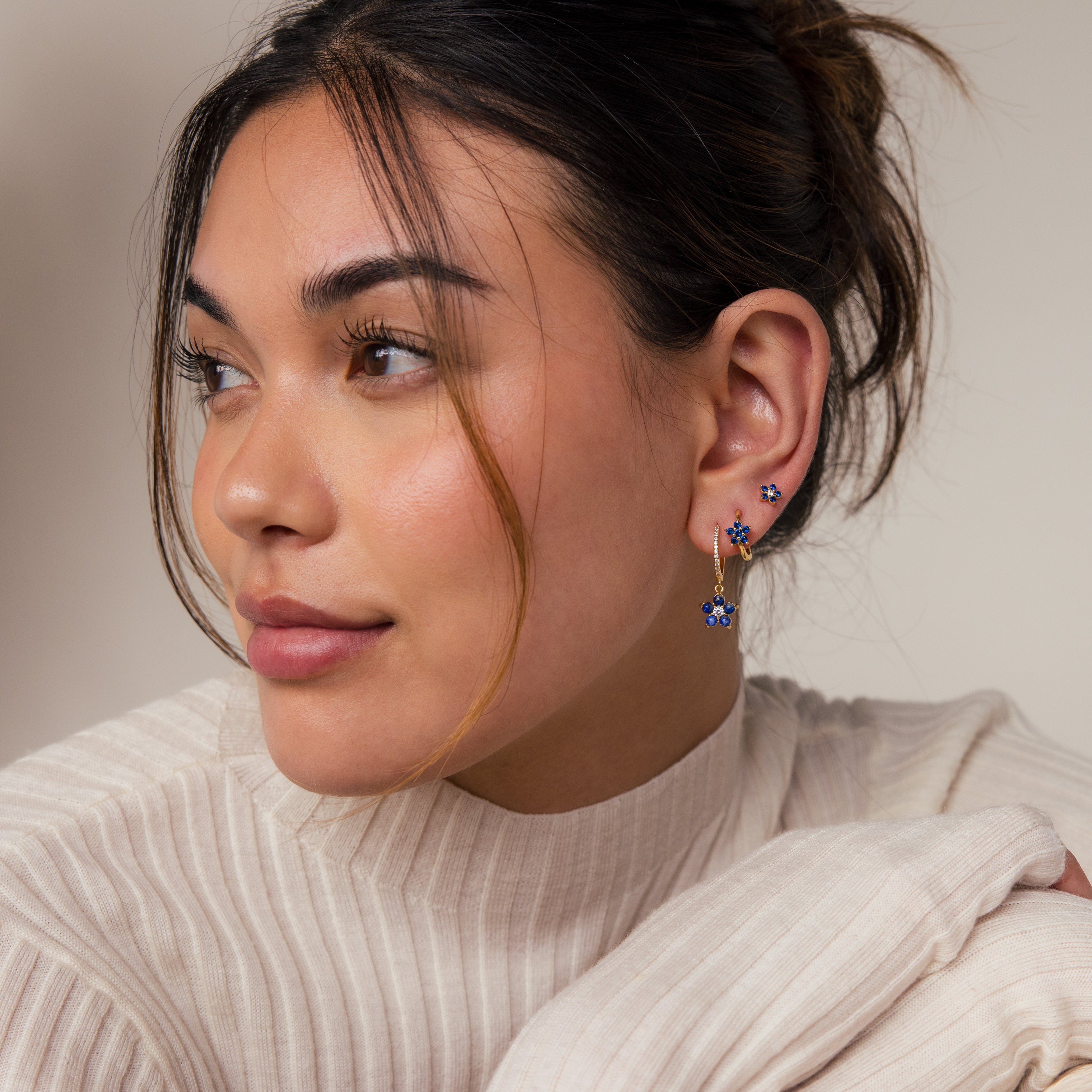 Woman with tied hair wearing a cream pleated top and Sapphire Flower Earrings Set - Silver, looking to the side.