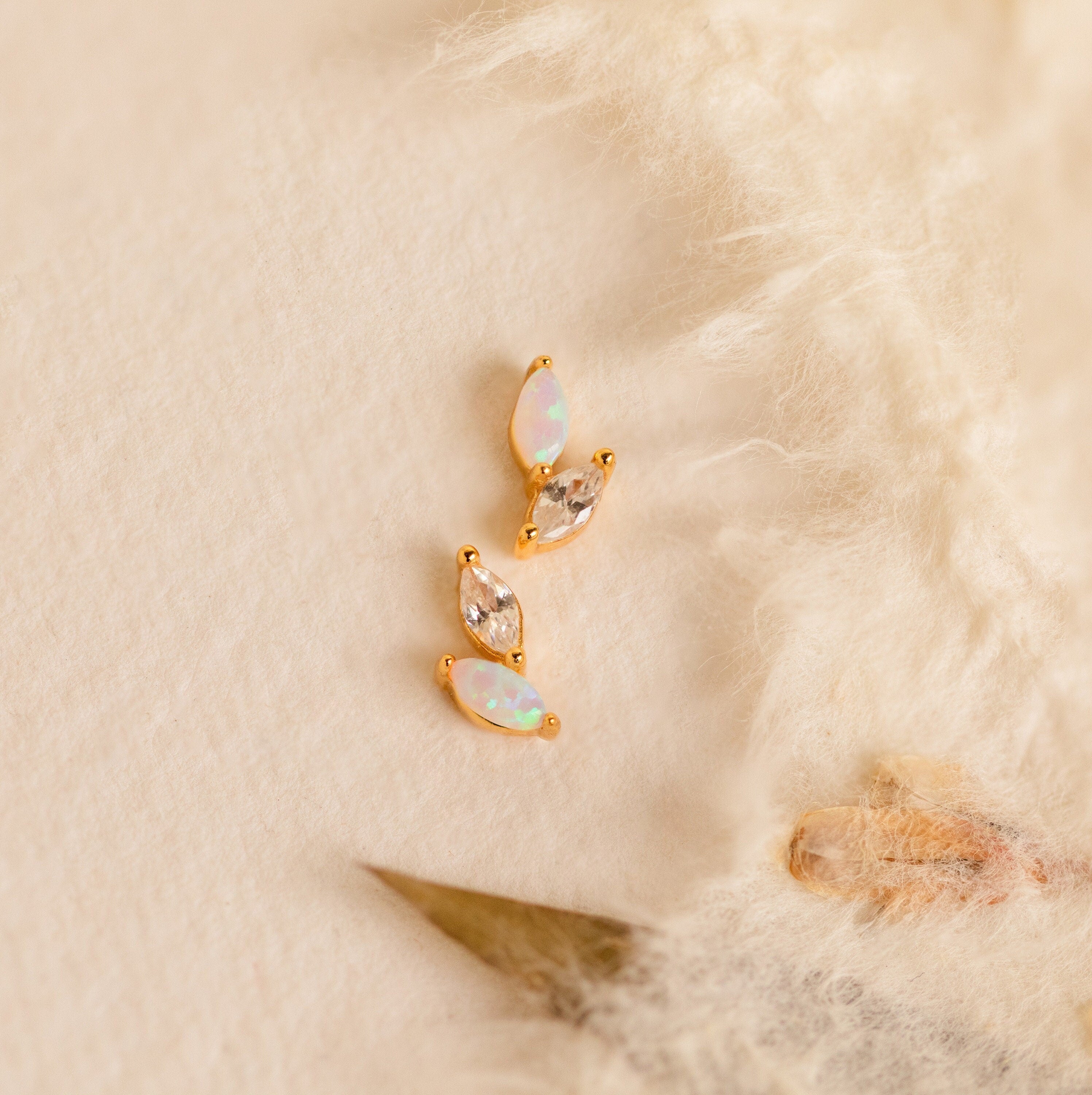 Three Opal & Diamond Marquise Studs, ideal as bridesmaid gifts or for lovers of mismatched earrings, are displayed on a soft cream-textured fabric background.
