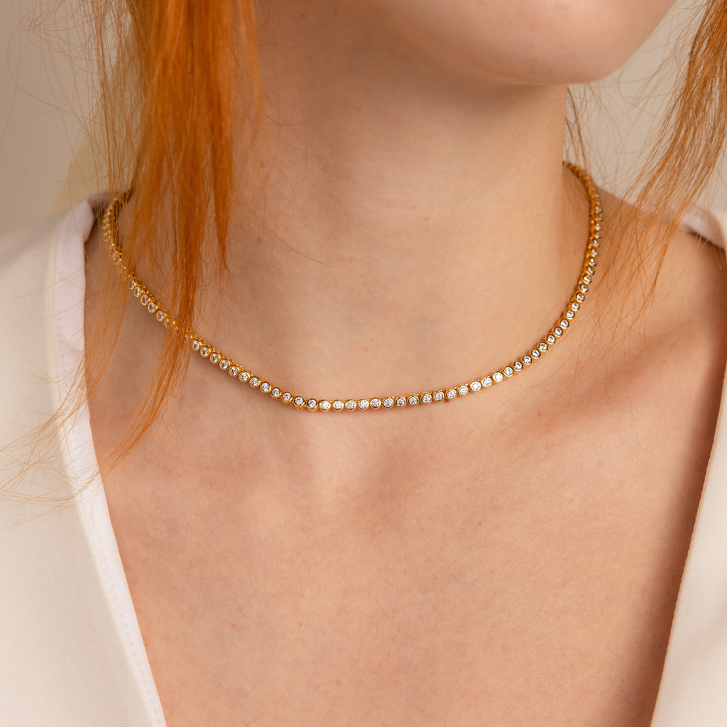 A woman wearing the Diamond Bezel Tennis Necklace with delicate small diamonds, shown from the shoulders up—an elegant piece ideal as a bridal necklace or a perfect gift for the bride.