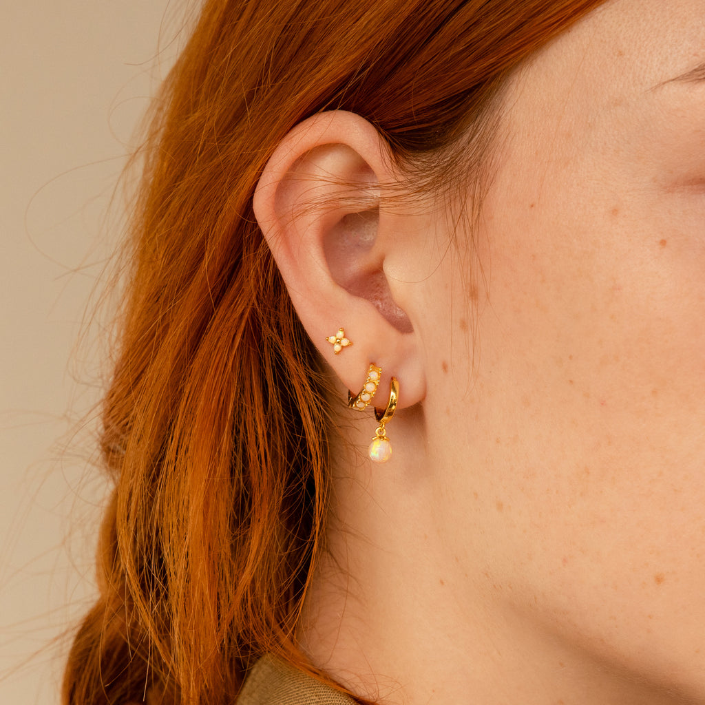 Close-up of a woman's ear with three gold earrings, including Opal Ivy Flower Studs and a small opal dangle. Her auburn hair peeks through, making this style a thoughtful gift for someone special.