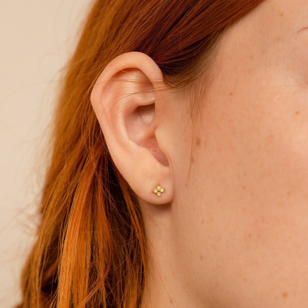 Close-up of a person's ear with red hair wearing a small gold flower-shaped earring from the Dainty Opal Stud Earrings Set—ideal for fans of minimalist jewelry or dainty opal studs.