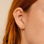Close-up of a person's ear with red hair wearing a small gold flower-shaped earring from the Dainty Opal Stud Earrings Set—ideal for fans of minimalist jewelry or dainty opal studs.