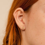 Close-up of a person's ear with Opal Ivy Flower Studs—a small gold flower earring—visible, with red hair in the background. A meaningful gift.