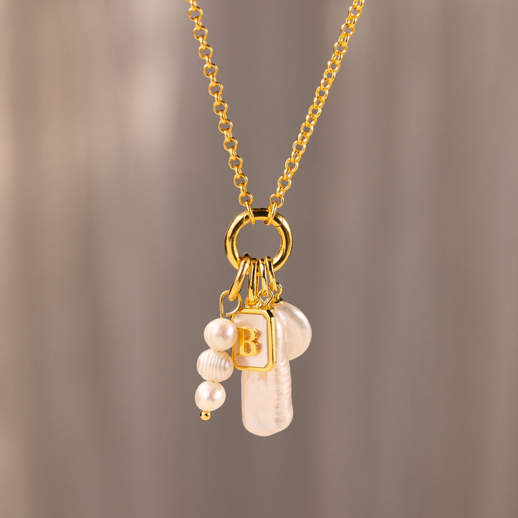 The Long Baroque Pearl Charm in 18K Gold features a gold chain, a Baroque pearl charm, and a gold square pendant with the letter B—a stunning addition to your pearl jewelry collection.