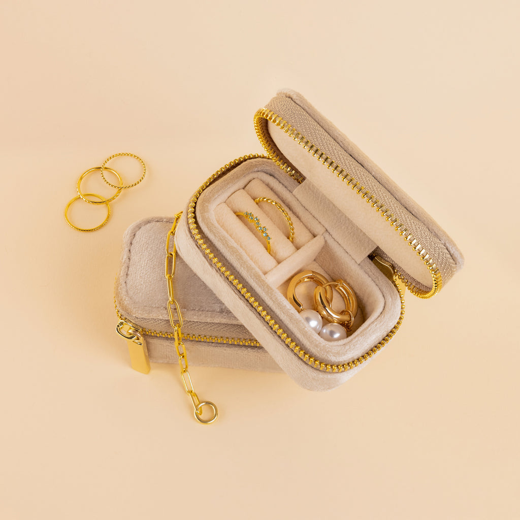 The Mini Travel Jewelry Box in beige velvet with a gold zipper is perfect for organizing rings and earrings while traveling; keep your bracelets nearby.