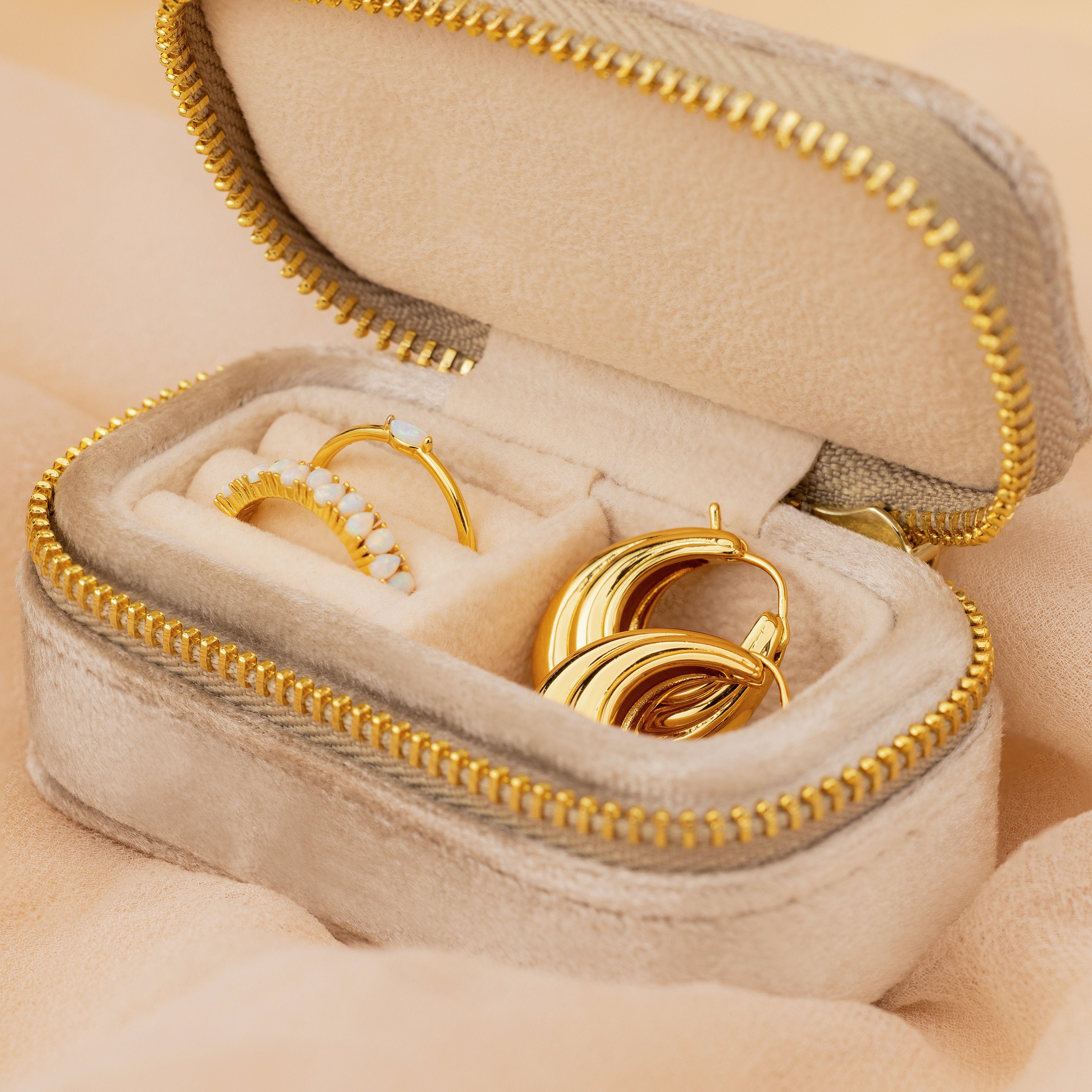 The Mini Travel Jewelry Box in beige velvet comes with gold earrings, a gold ring, and a pearl ring inside—an ideal compact organizer for jewelry on your trips.