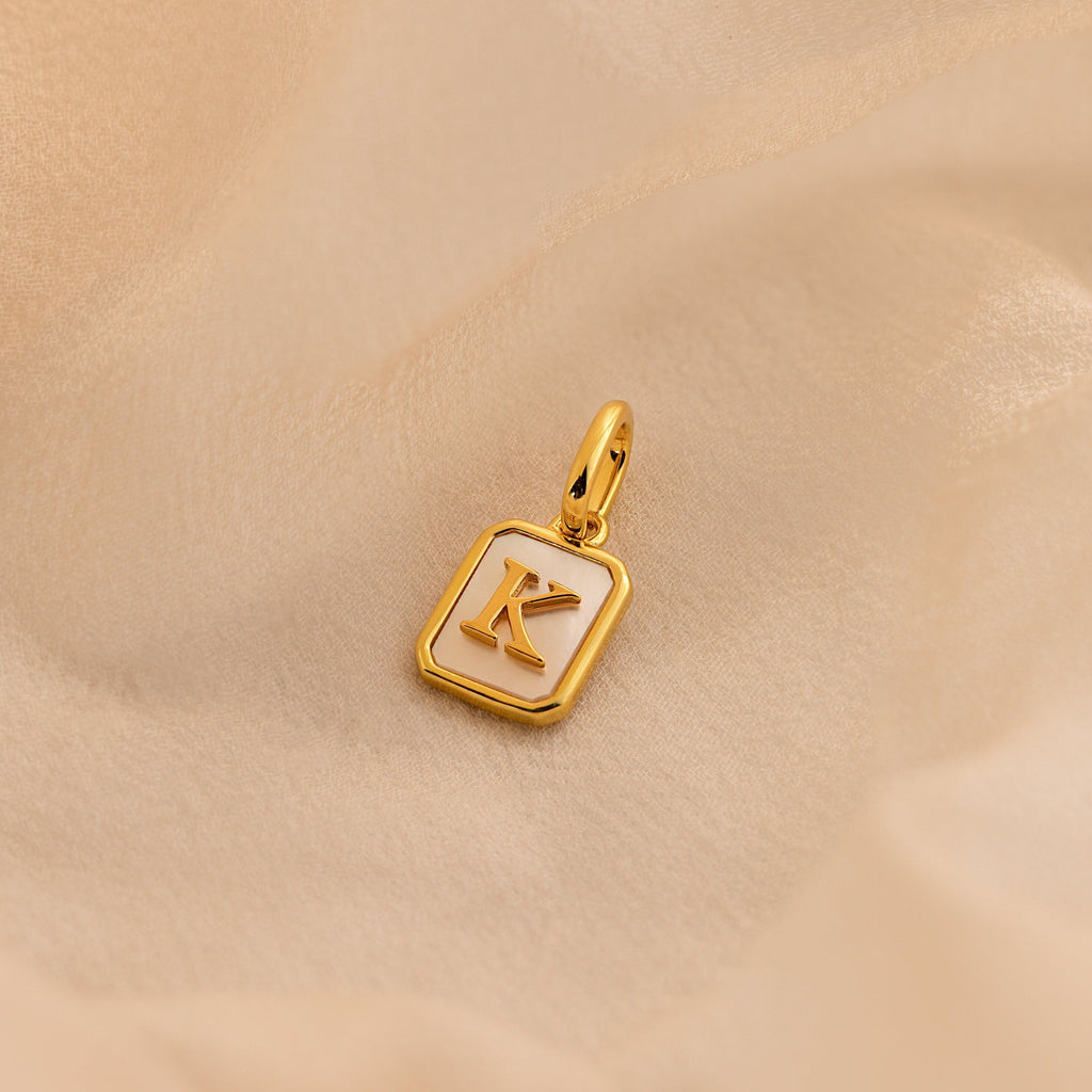 Gold Mother of Pearl Initial Charm with Letter K, featuring a rectangular pearl base with rounded gold corners, a large jump ring, and an initial in times new roman.