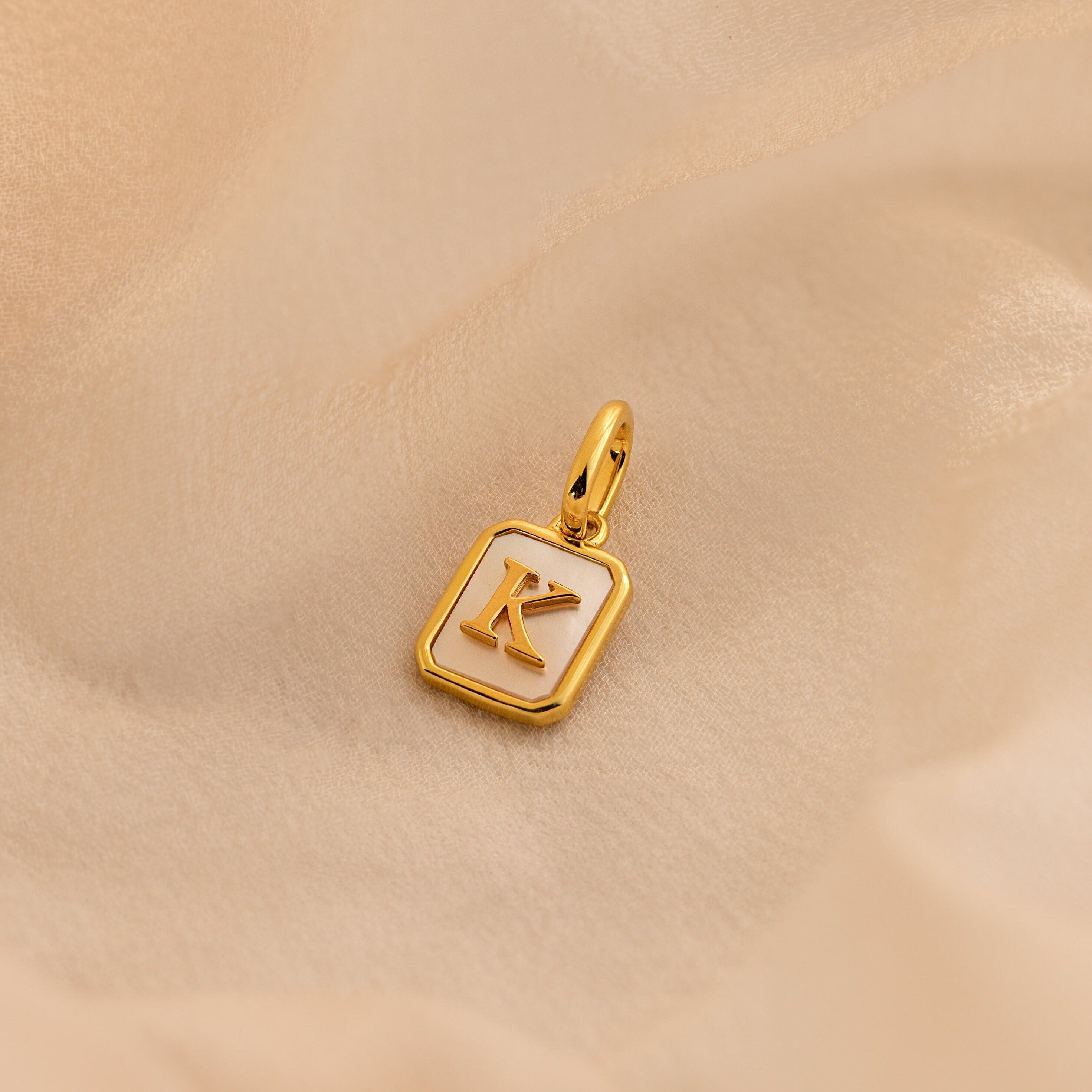 Gold Mother of Pearl Initial Charm with Letter K, featuring a rectangular pearl base with rounded gold corners, a large jump ring, and an initial in times new roman.