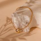 Rolo Circle Charm Bracelet in 18K Gold with a detachable hinged circle for adding charms. Shown on a textured beige stone against a neutral background.