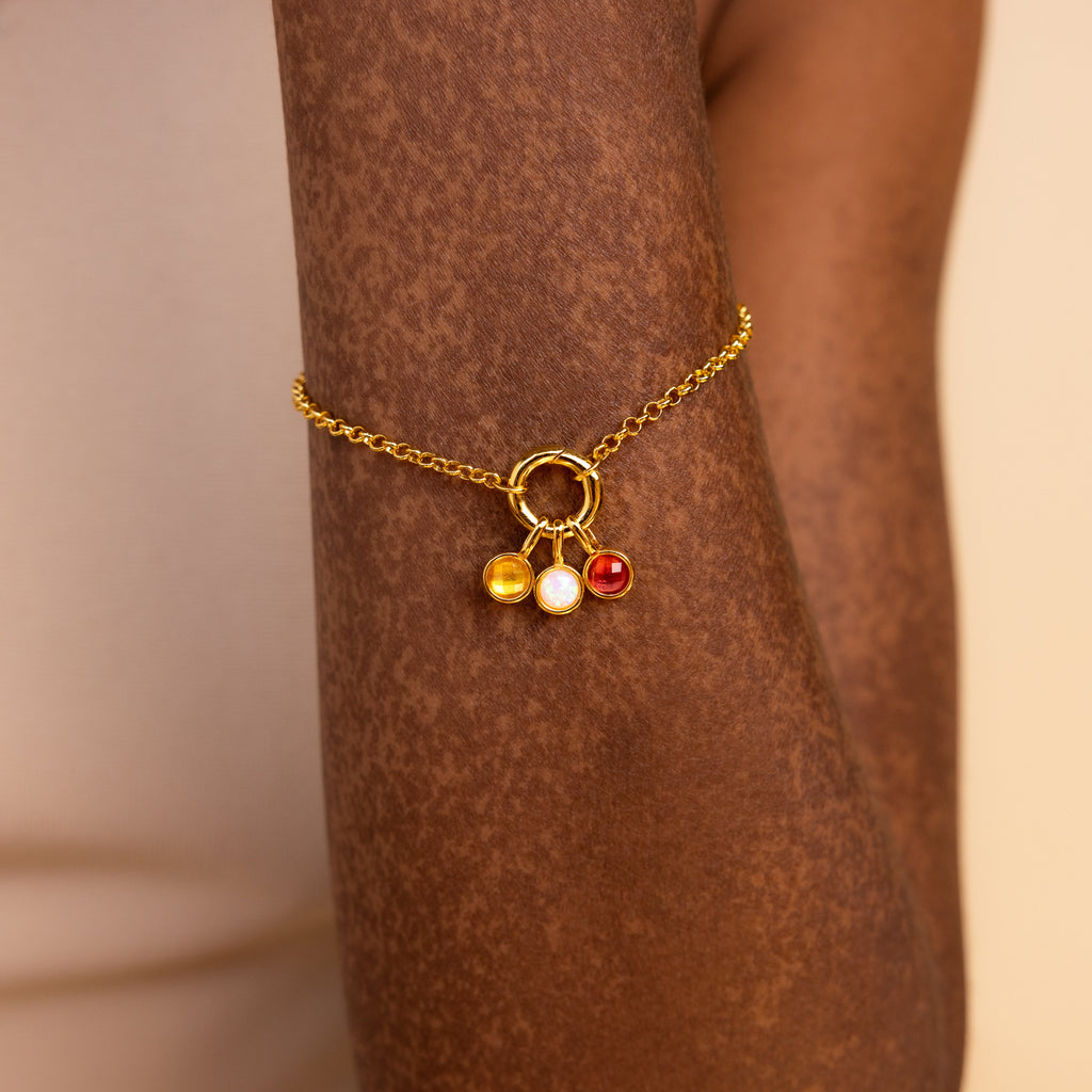 Model wears gold rolo charm bracelet with topaz, opal and garnet signet charms