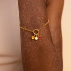 Model wears gold rolo charm bracelet with topaz, opal and garnet signet charms