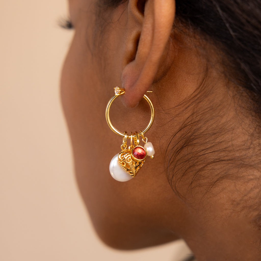 Model wears a large hoop earring with a signet garnet charm, heart charm and two pearl charms. 