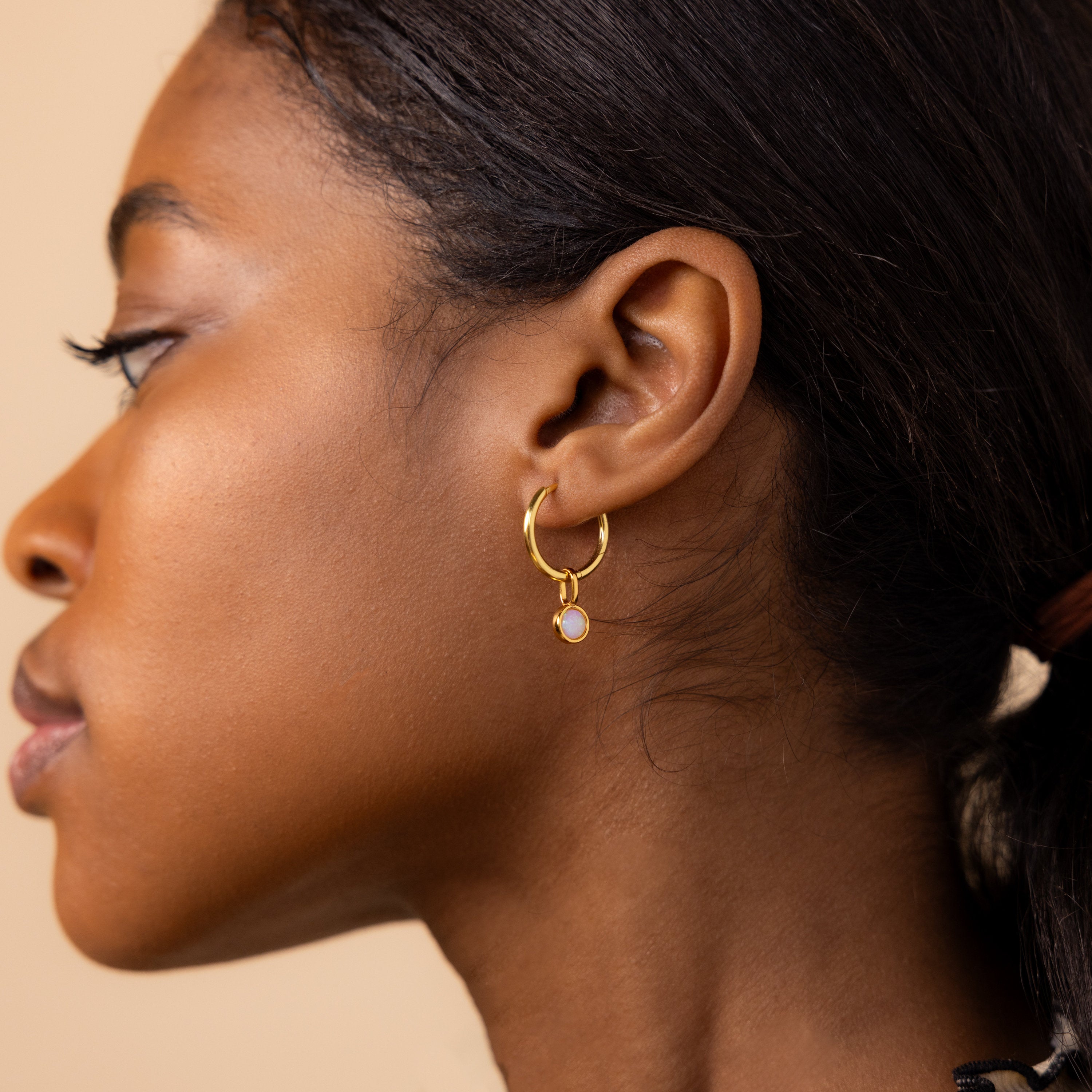 Model wears large hoop earring with a dangling signet opal charm attached to it. 