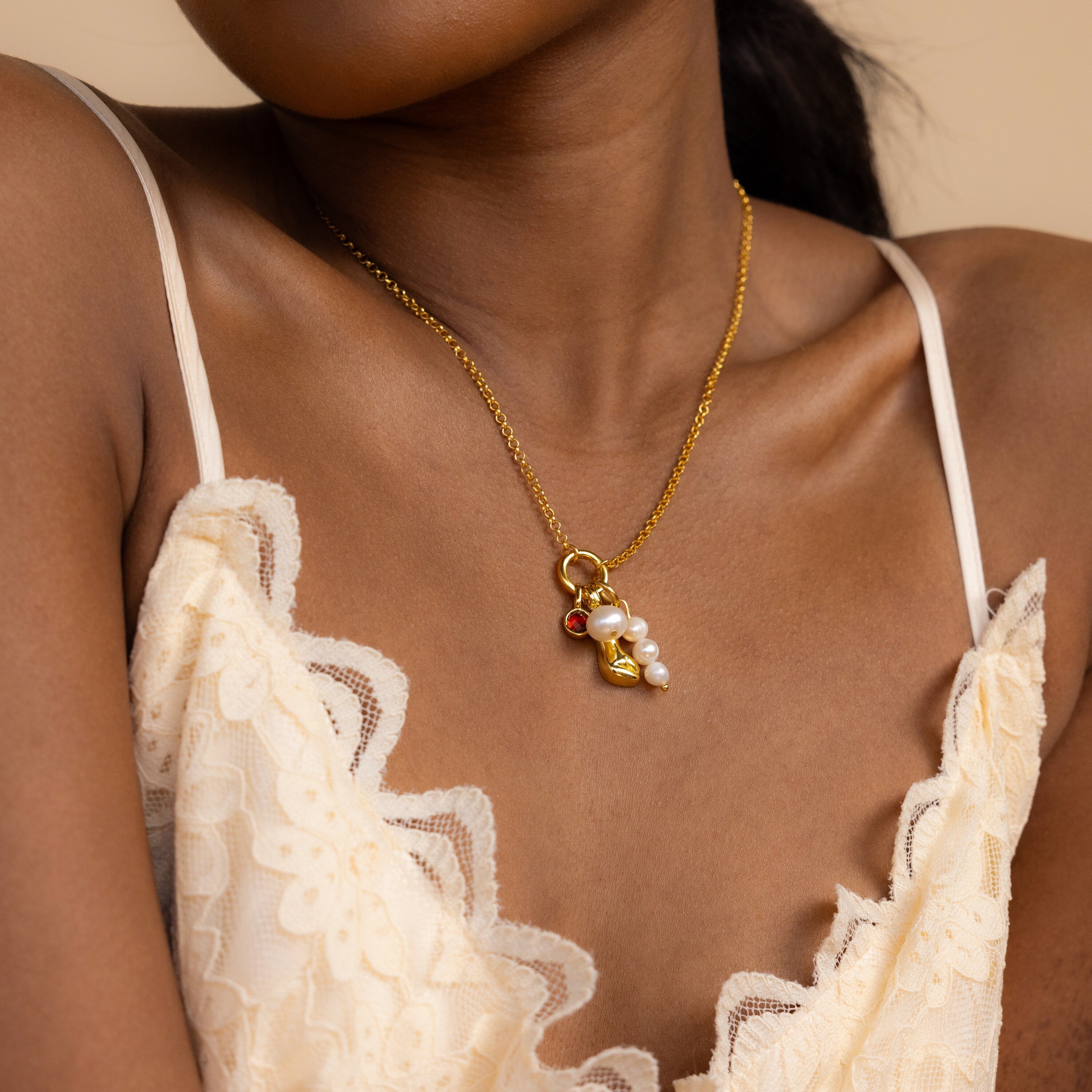 A woman in a cream lace dress wears the Classic Pearl Charm in 18K Gold, featuring colorful charms and pearls, paired beautifully with a delicate hoop earring.