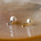 The Classic Pearl Charm in Sterling Silver, perfect as a pendant or for adding to a hoop earring, rests on a shiny, iridescent surface.