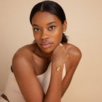 Woman with natural makeup wears the Rolo Circle Charm Bracelet in 18K Gold, featuring a detachable hinged circle perfect for adding charms and personalizing your style, resting her chin on her hand against a beige background.