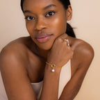 A woman with dark hair and smooth skin elegantly poses wearing the Rolo Circle Charm Bracelet in 18K Gold, featuring a detachable hinged circle—perfect for adding charms and personalizing her look.