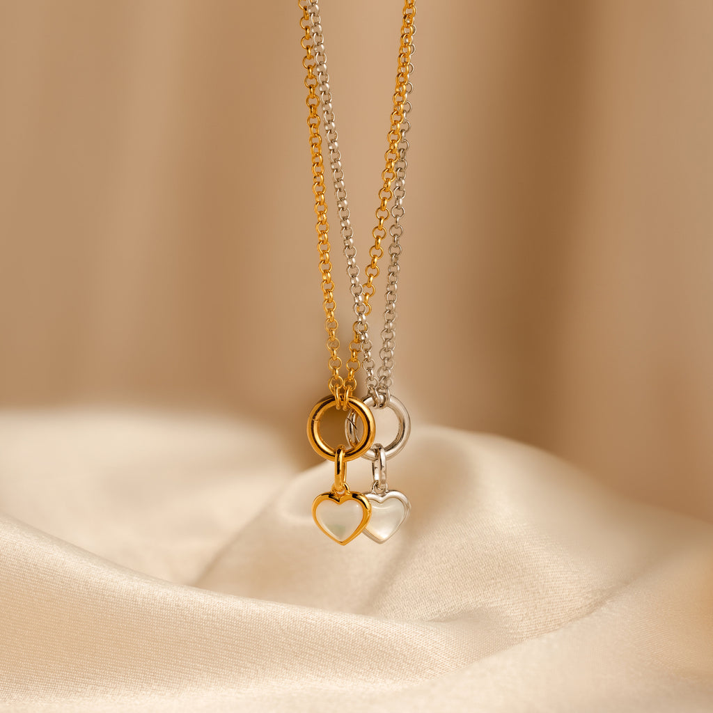 A Mother of Pearl Heart Charm in Sterling Silver necklace is displayed on smooth beige fabric, offering a touch of vintage-inspired elegance.