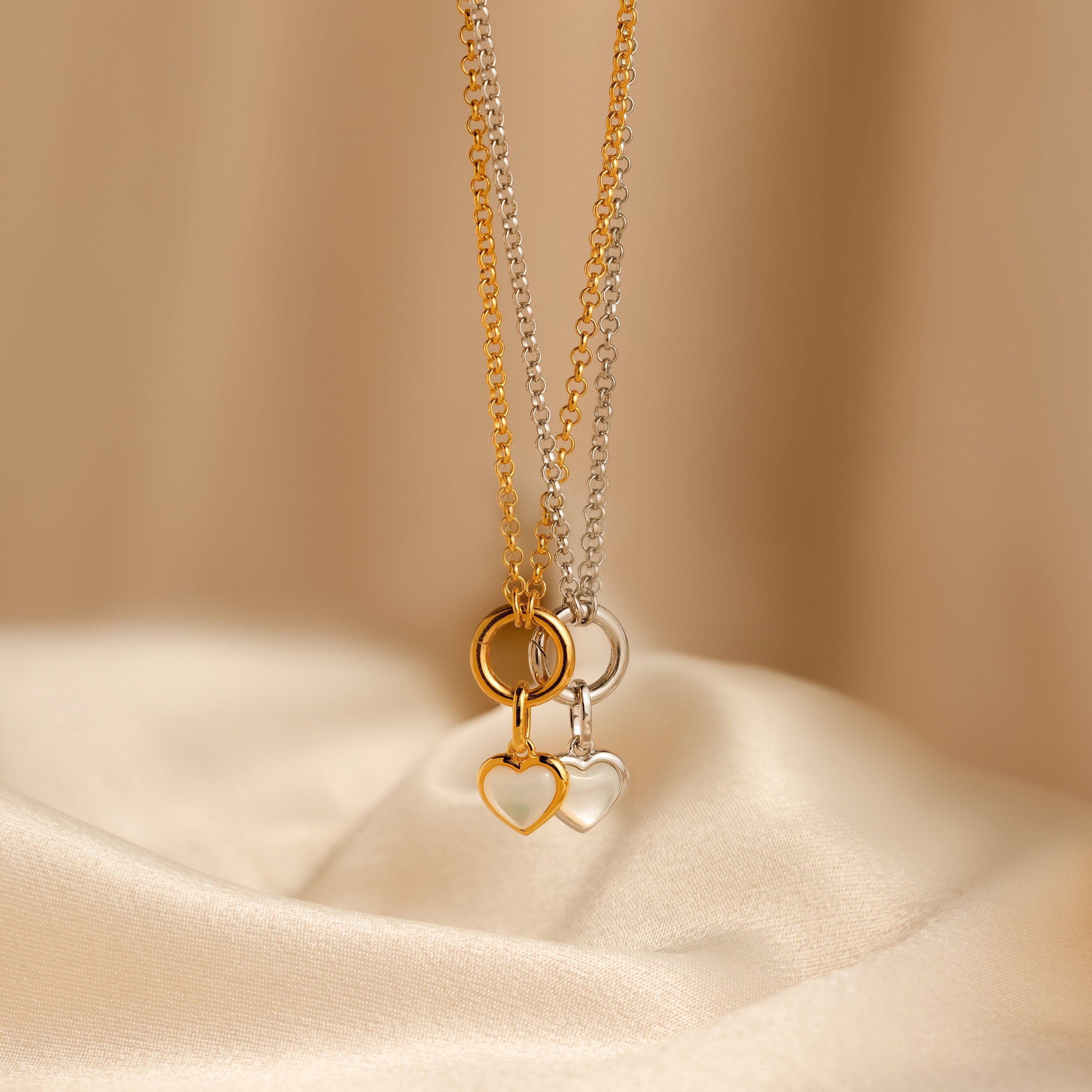 A Mother of Pearl Heart Charm in Sterling Silver necklace is displayed on smooth beige fabric, offering a touch of vintage-inspired elegance.