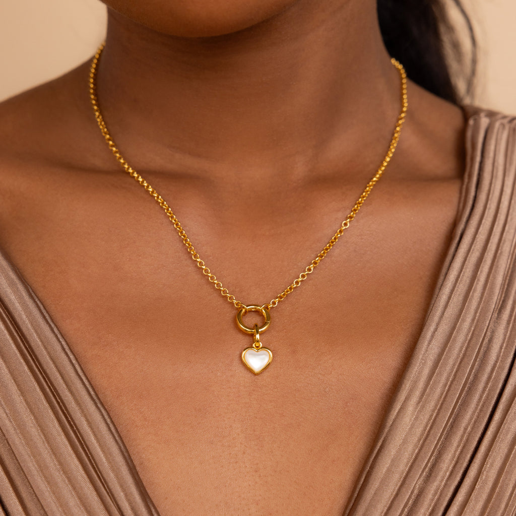 A woman wears the Mother of Pearl Heart Charm necklace, paired with a taupe v-neck top.