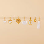 Eight vintage jewelry charms, featuring the Mother of Pearl Heart Charm, are arranged in a row on a beige background.