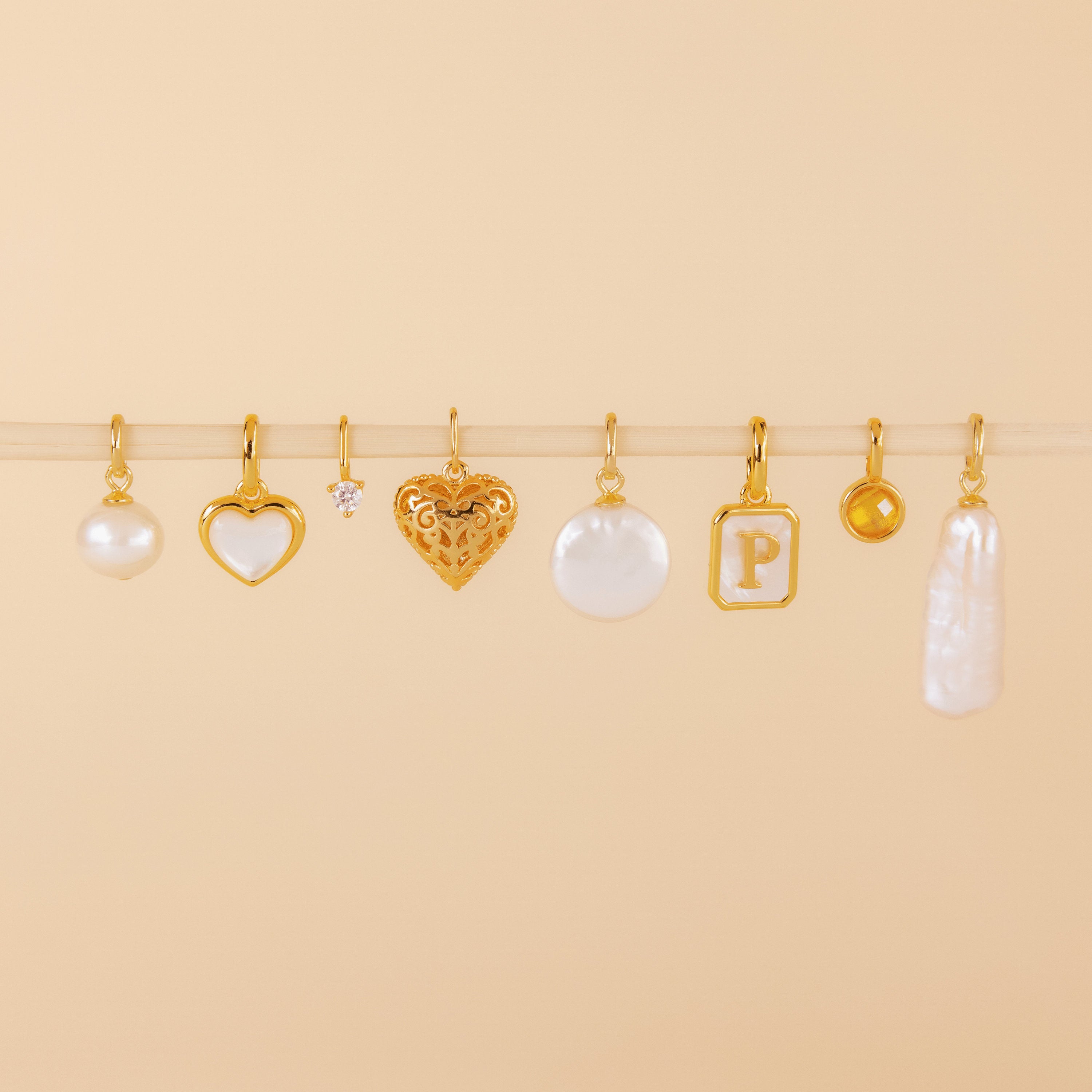 Eight vintage jewelry charms, featuring the Mother of Pearl Heart Charm, are arranged in a row on a beige background.