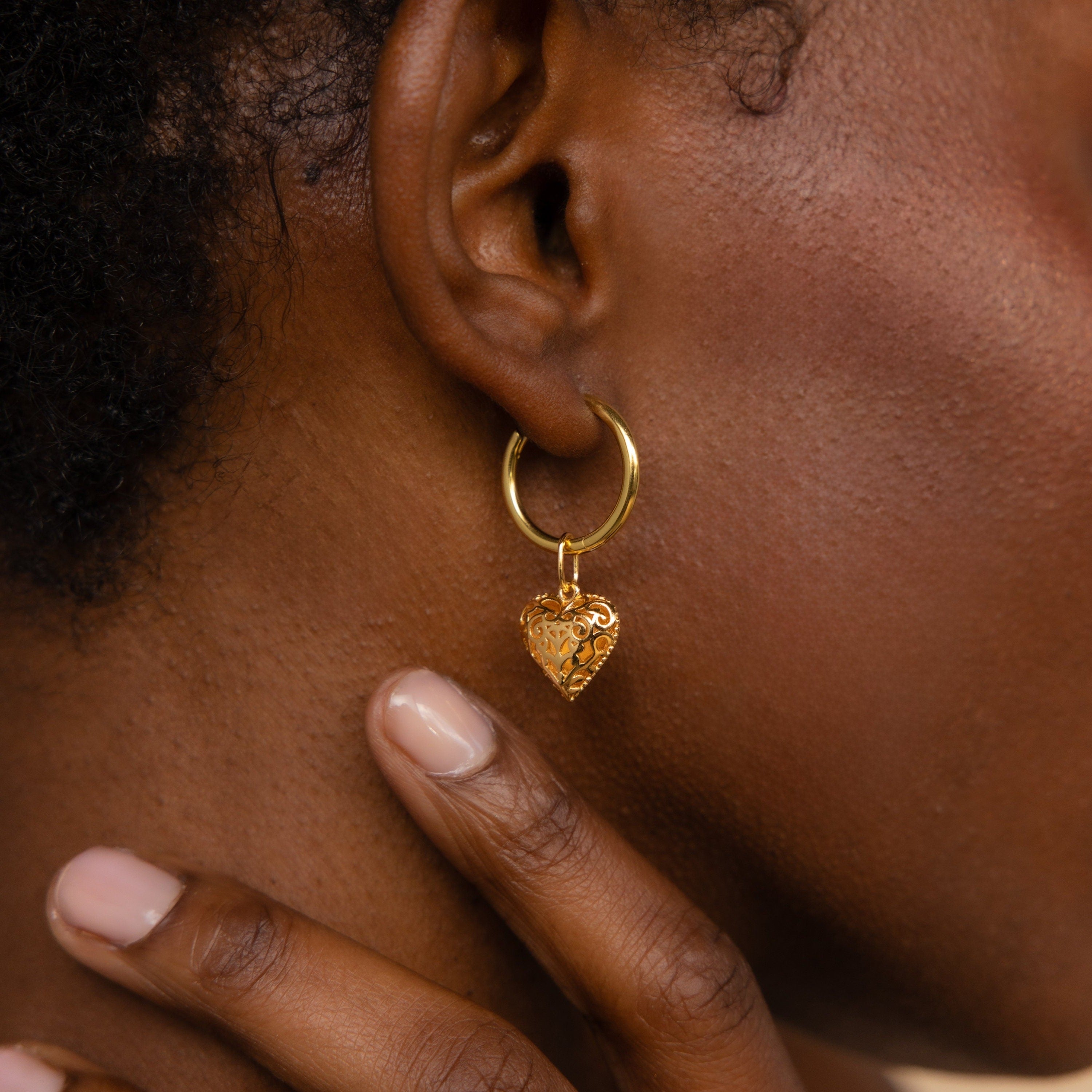 Close-up of a person wearing the Vintage Heart Charm gold hoop earring, hand touching their neck—a timeless piece for any jewelry collection.