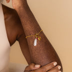 The Vintage Heart Charm in 18K Gold features a pearl and red gem, shown on a person’s arm with vitiligo against a beige background—a timeless piece for any jewelry collection.