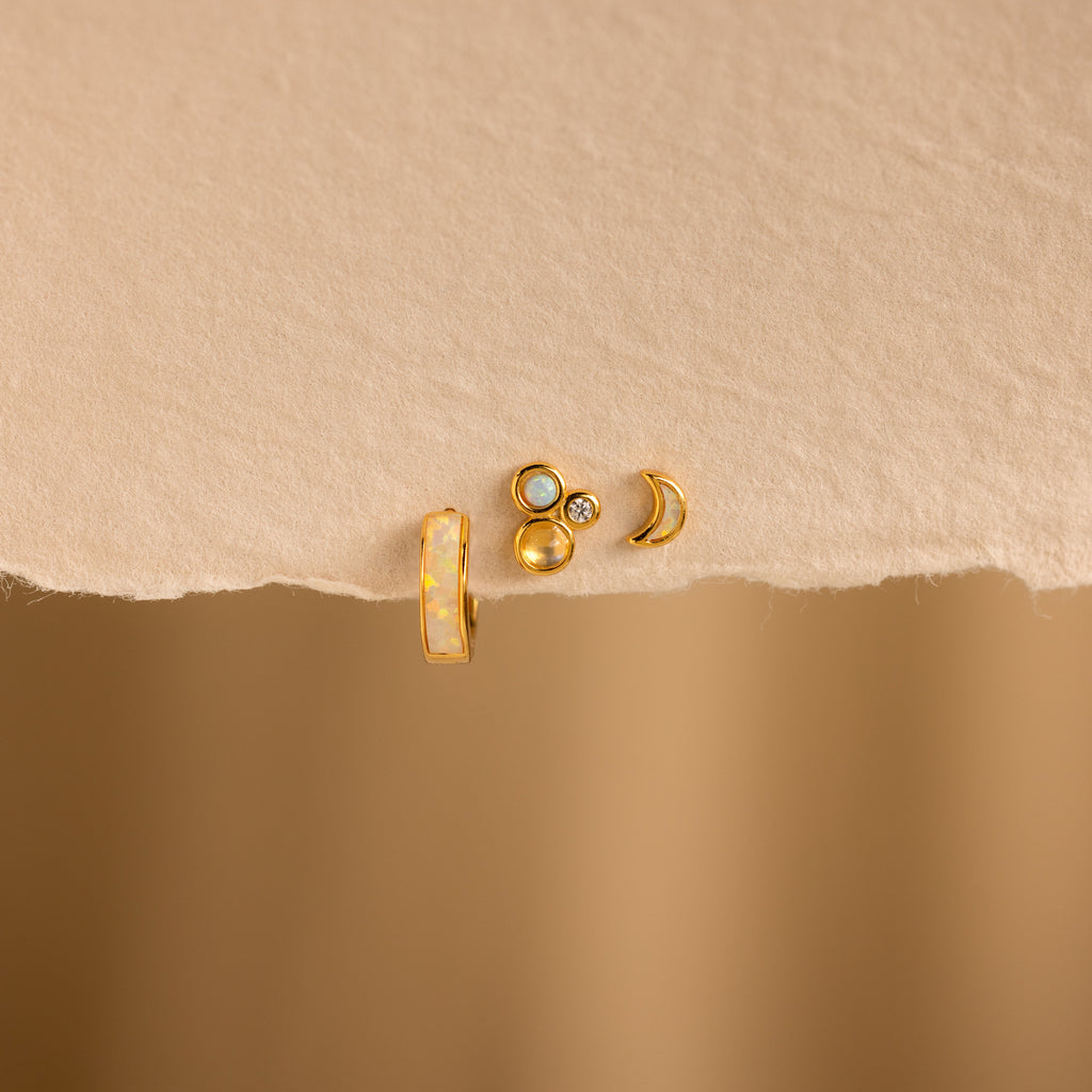 The Opal Inlay Earrings Set features four small gold stud earrings in varied shapes, displayed on textured beige paper with a blurred tan background—an elegant jewelry gift for her.