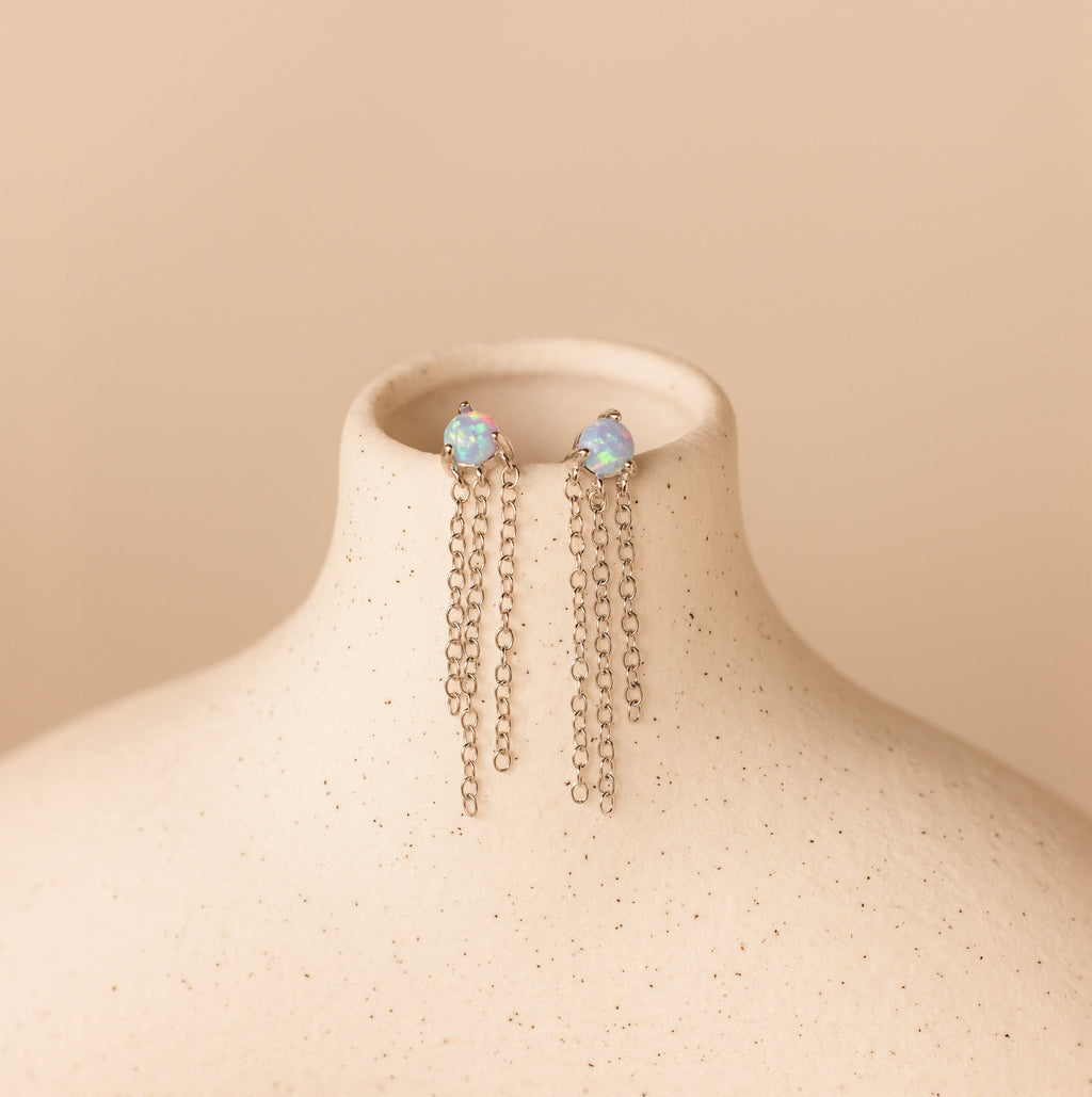 Opal Chain Earrings with opal stone studs and long silver chains, beautifully displayed on a light beige textured jewelry stand—a stunning addition to your collection.