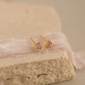 Pink Baguette Opal Studs: Elegant gold stud earrings with rectangular pink tourmaline stones and small opal accents, beautifully displayed on soft fabric and textured stone—the perfect choice for bridal gifts.
