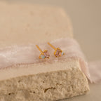 Pink Baguette Opal Studs: Elegant gold stud earrings with rectangular pink tourmaline stones and small opal accents, beautifully displayed on soft fabric and textured stone—the perfect choice for bridal gifts.