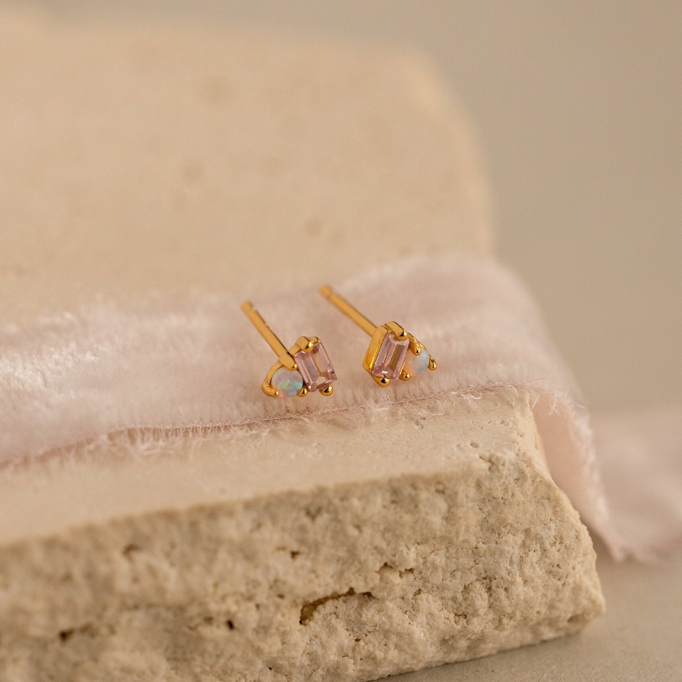 Pink Baguette Opal Studs: Elegant gold stud earrings with rectangular pink tourmaline stones and small opal accents, beautifully displayed on soft fabric and textured stone—the perfect choice for bridal gifts.