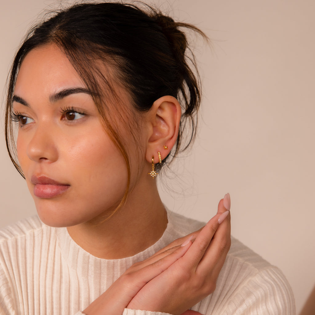 Woman with tied-back hair wears the Opal Starburst Earrings Set and a cream ribbed top, looking to the side.