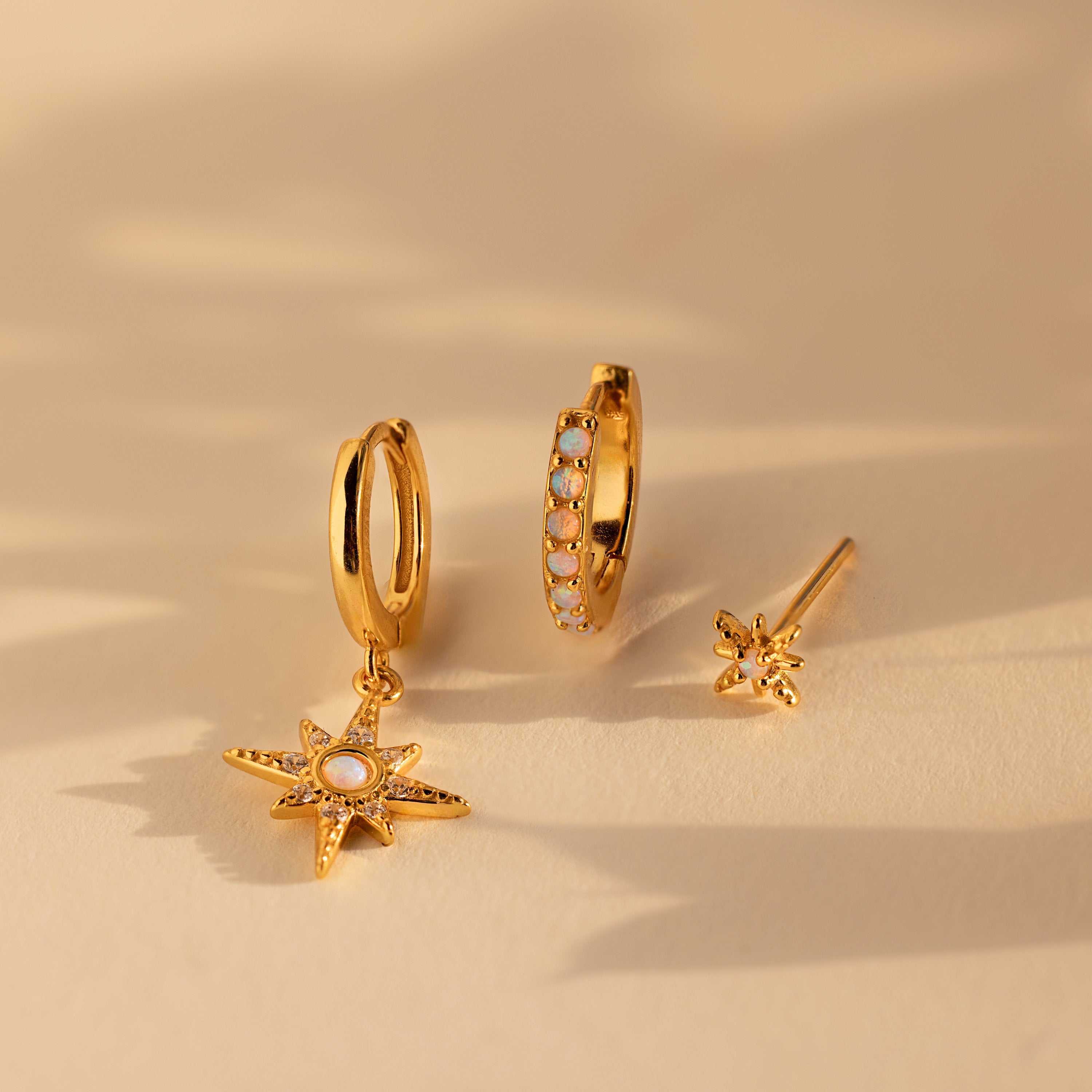 Showcasing the Opal Starburst Earrings Set: includes one hoop with a star charm, one gem-accented hoop, and a small star-shaped stud—a sparkling upgrade to any jewelry collection.
