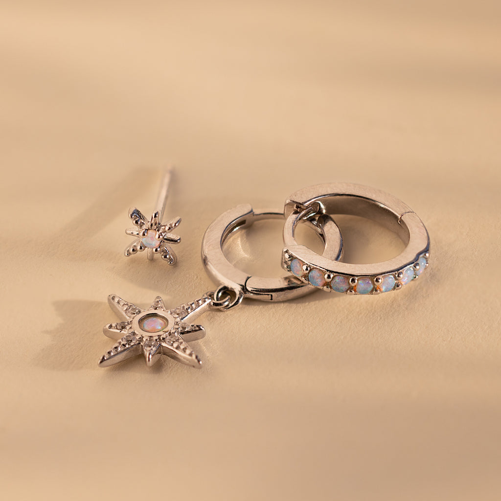 The Opal Starburst Earrings Set, featuring three silver earrings with star and gemstone details, is displayed on a beige background for a dazzling effect.