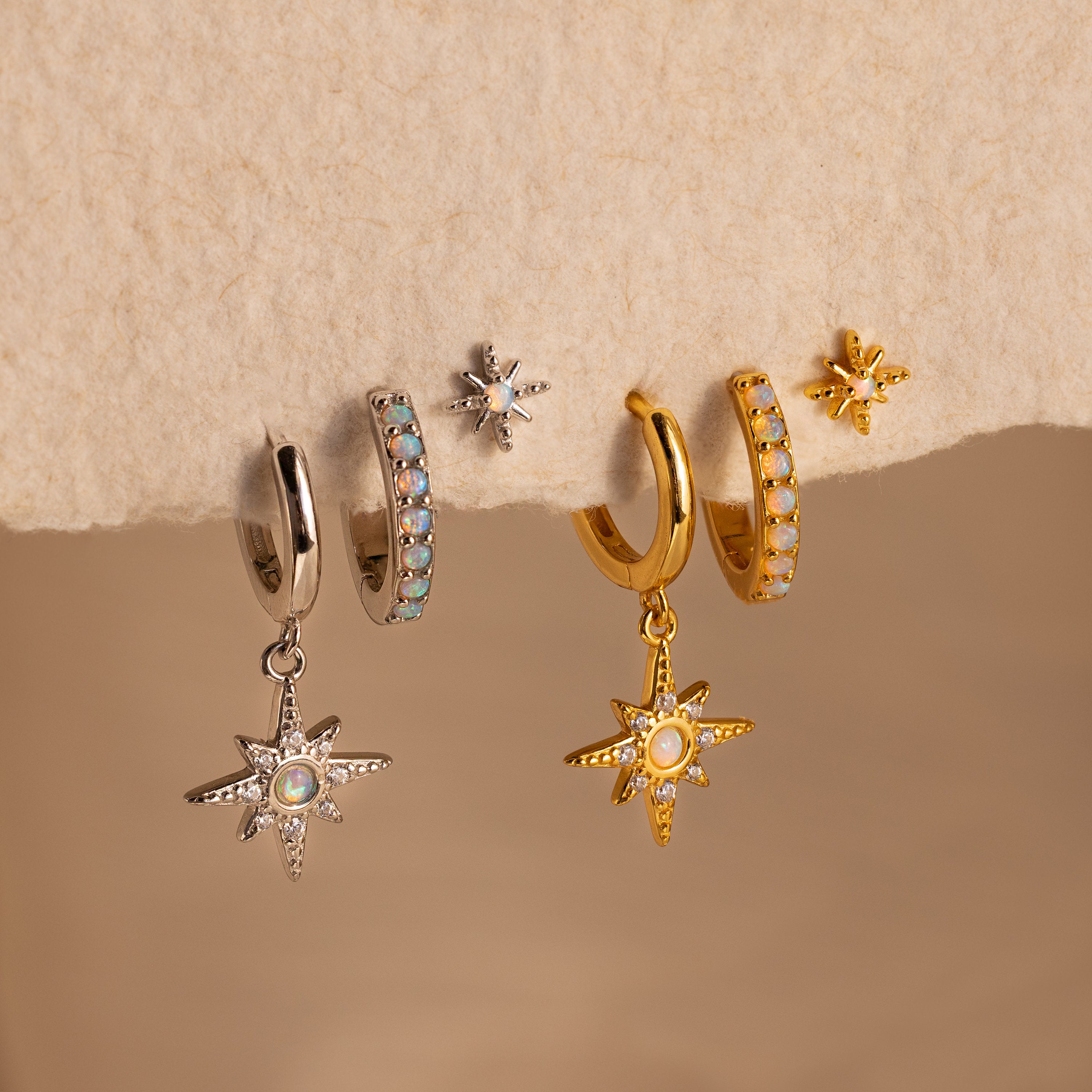 The Opal Starburst Earrings Set features five stunning silver and gold-tone pairs, beautifully arranged on a soft beige surface.
