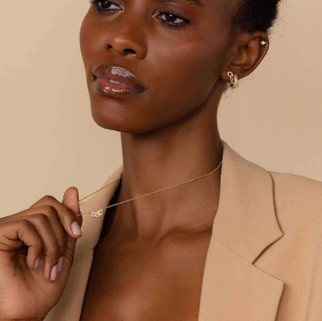 A woman in a beige blazer showcases the Pave Link Necklace from the jewelry collection, paired with gold hoop earrings, against a neutral background.