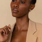 A woman in a beige blazer showcases the Pave Link Necklace from the jewelry collection, paired with gold hoop earrings, against a neutral background.