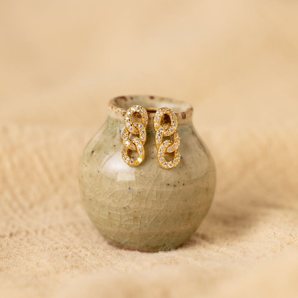 The Pave Link Studs are displayed on a small, textured ceramic vase against a beige background.