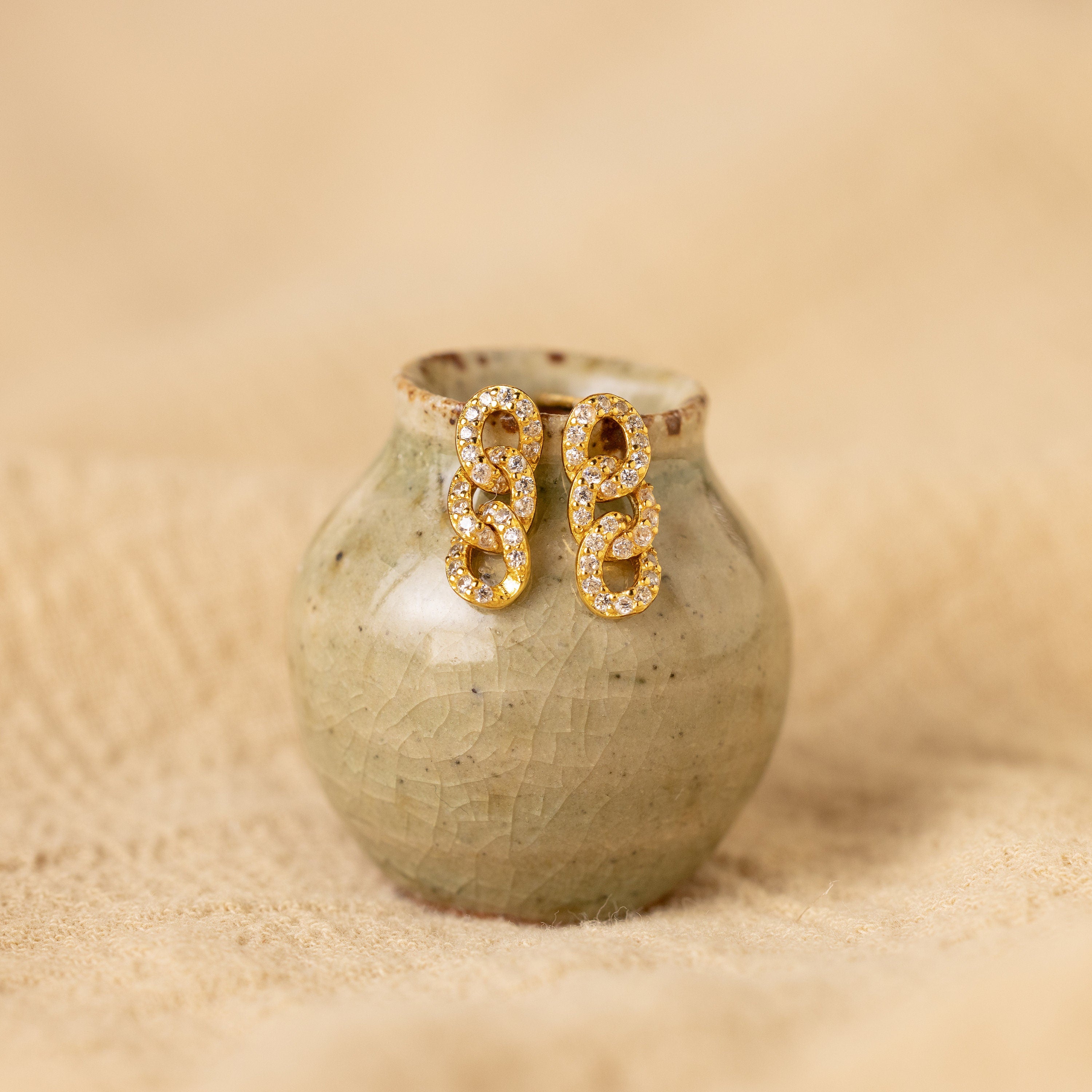 The Pave Link Studs are displayed on a small, textured ceramic vase against a beige background.