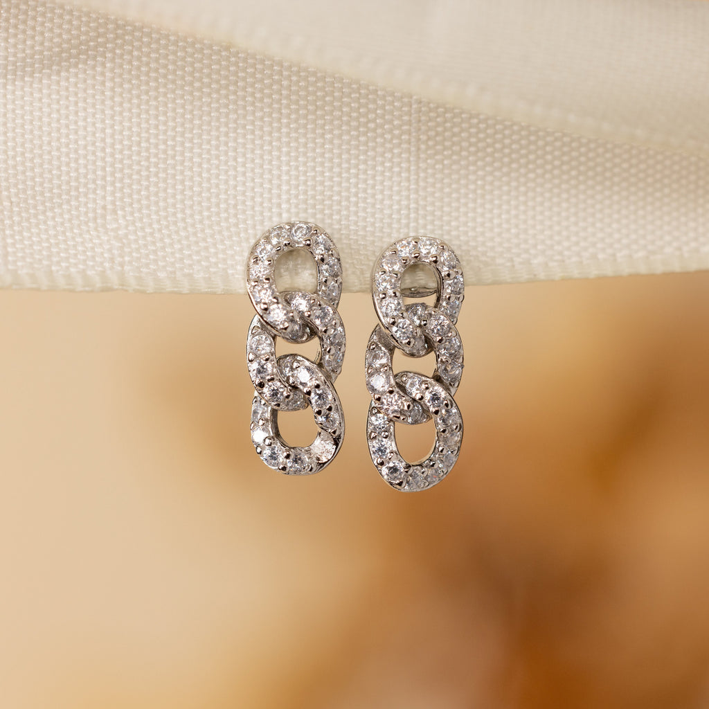 Elegant Pave Link Studs featuring three interlocking loops, each adorned with sparkling stones, rest on cream fabric—a timeless tribute to classic style.