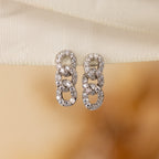 Elegant Pave Link Studs featuring three interlocking loops, each adorned with sparkling stones, rest on cream fabric—a timeless tribute to classic style.