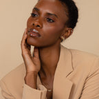 Woman in a beige blazer poses with her hand on her face, wearing elegant Pave Link Studs and a sparkling diamond necklace.