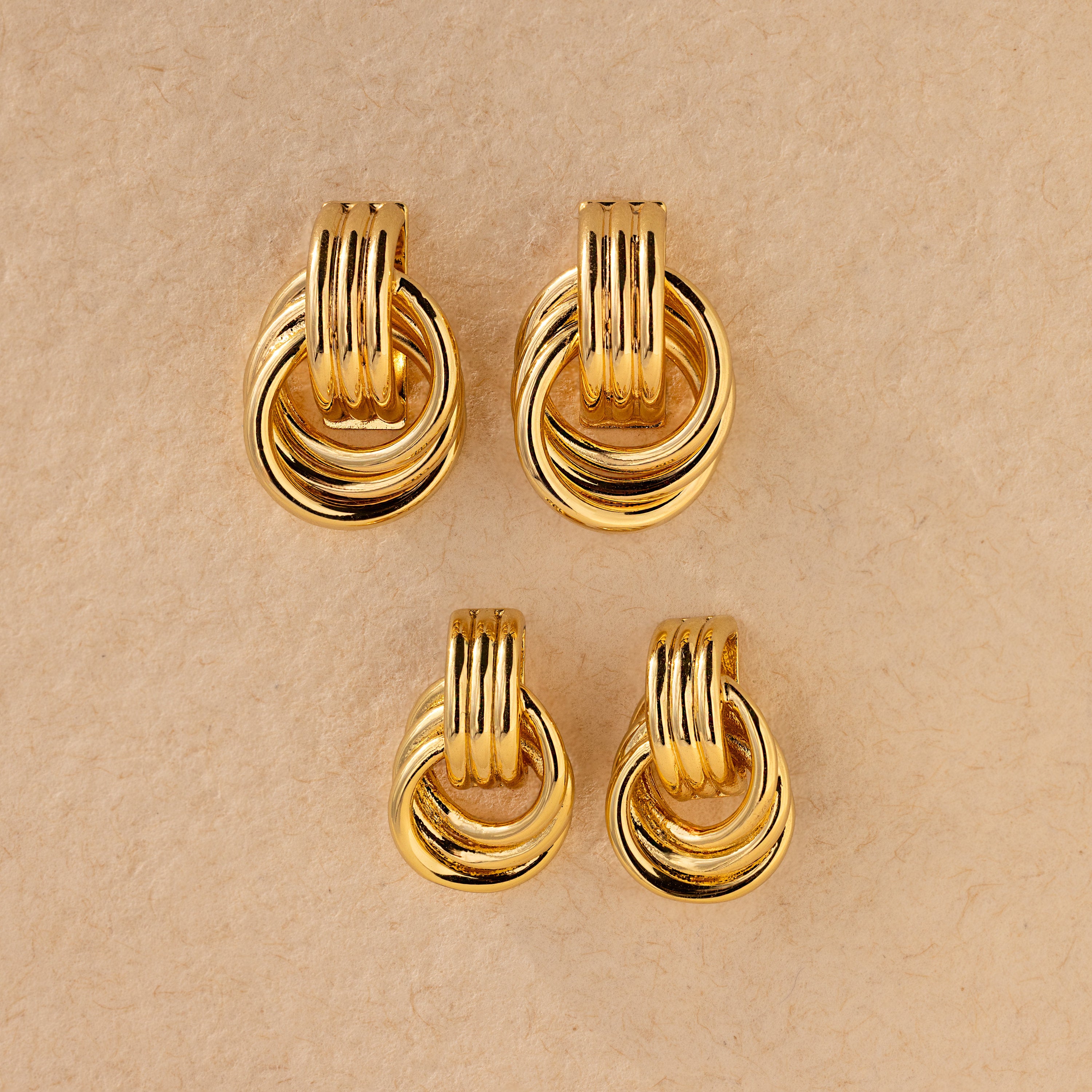 Four pairs of elegant earrings, featuring the Triple Knot Earrings with interlocking circles, displayed on a beige textured background—perfect as an anniversary gift.