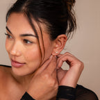 Woman with dark hair in a bun adjusts the Marquise Diamond Earrings Set, wearing a sheer black top and looking to the side—an elegant look perfect for wedding inspiration and thoughtful bridesmaid gifts.