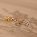 The Marquise Diamond Earrings Set, featuring gold and silver with gemstones, is displayed on a beige surface, exuding wedding elegance amid soft shadows in the background.