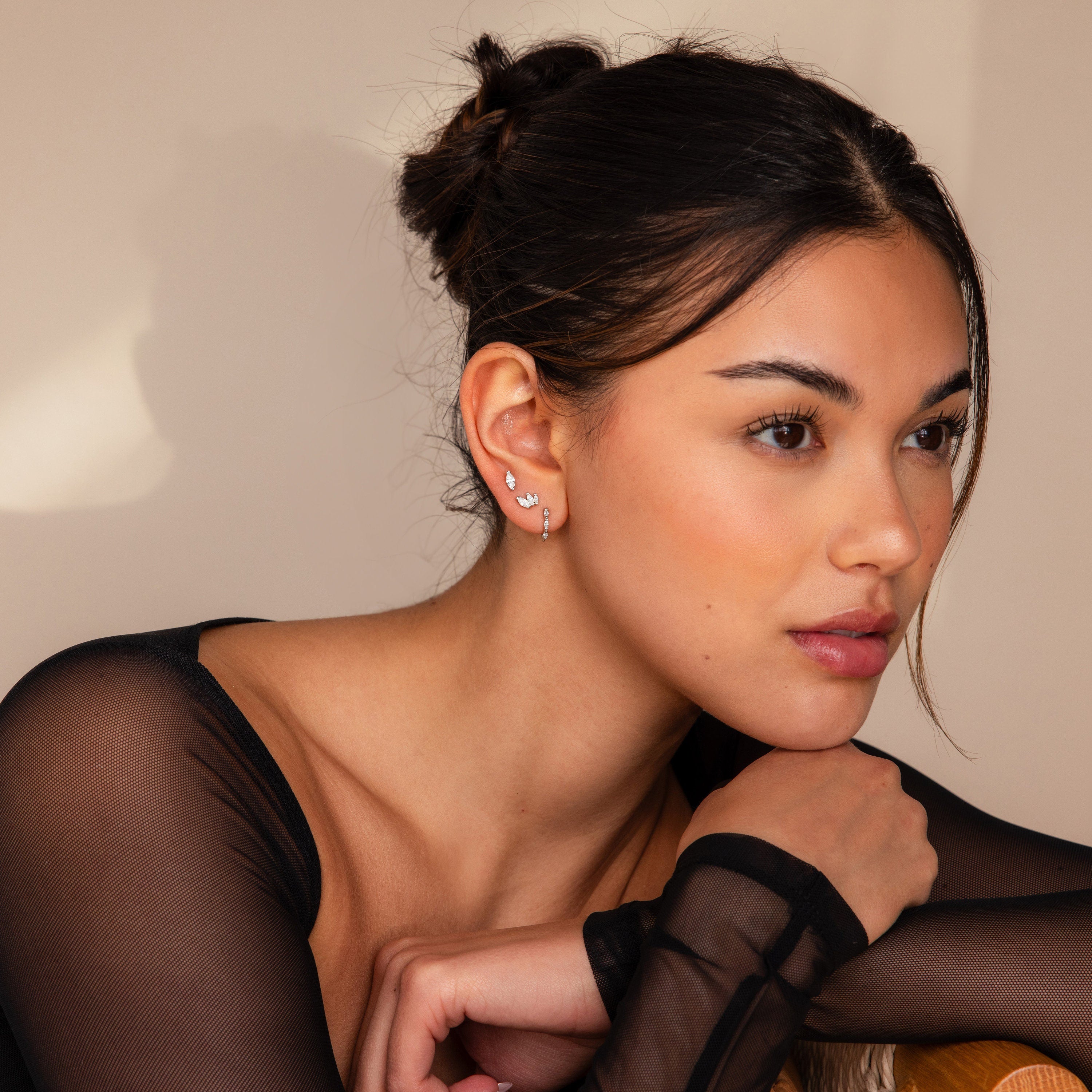 A woman with dark hair in a bun, wearing a sheer black top and the Marquise Diamond Earrings Set, gazes thoughtfully—a perfect portrait of wedding elegance.