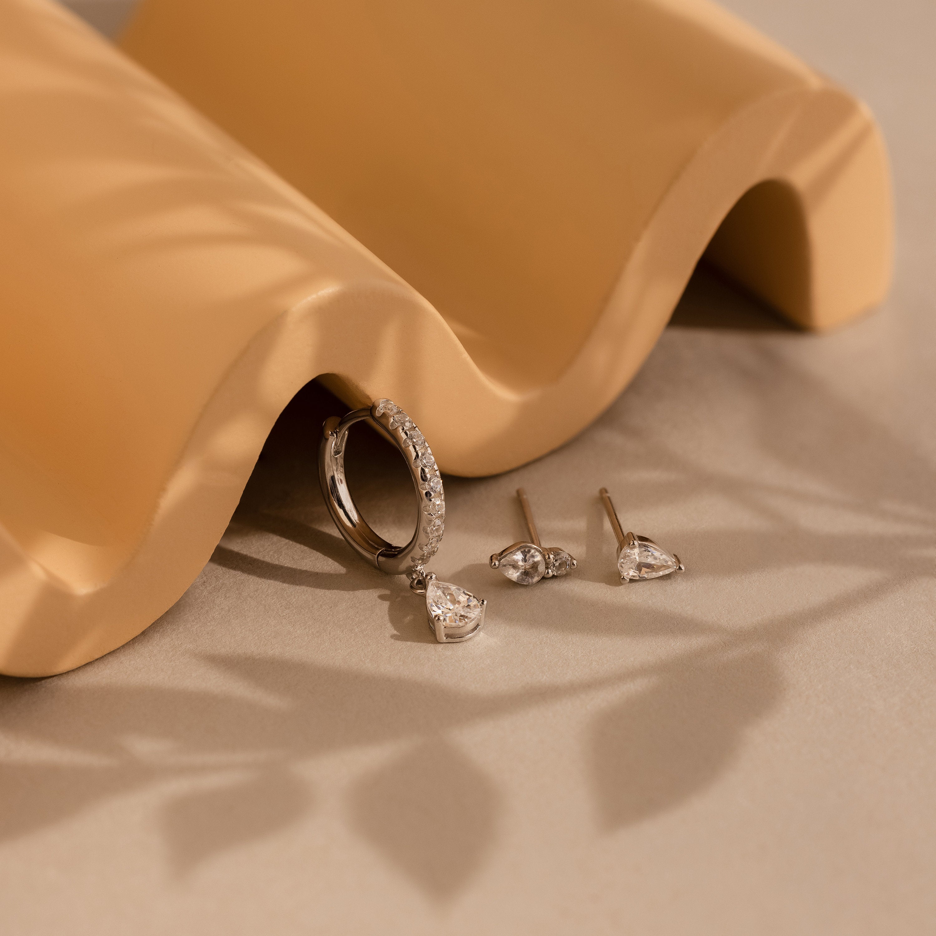Diamond Drop Earrings Set displayed on a beige wavy surface with soft shadows.